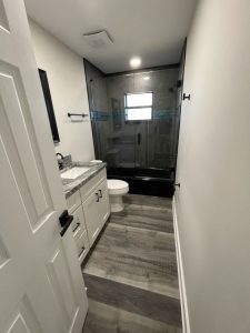 Remodeled bathroom with white vanity and dark tiled shower