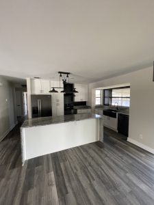 Remodeled kitchen island with white cabinets and black range hood